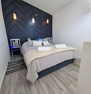 A modern bedroom with a herringbone-patterned headboard, a bed with white linens, and a nightstand with a lamp.
