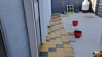 Un estrecho sendero exterior con un diseño de baldosas en damero que conduce a la entrada de un edificio.