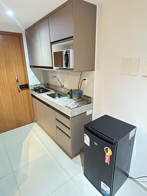 Eine kleine Küche mit integriertem Mikrowellenherd, einer Spüle und einem schwarzen Kühlschrank.