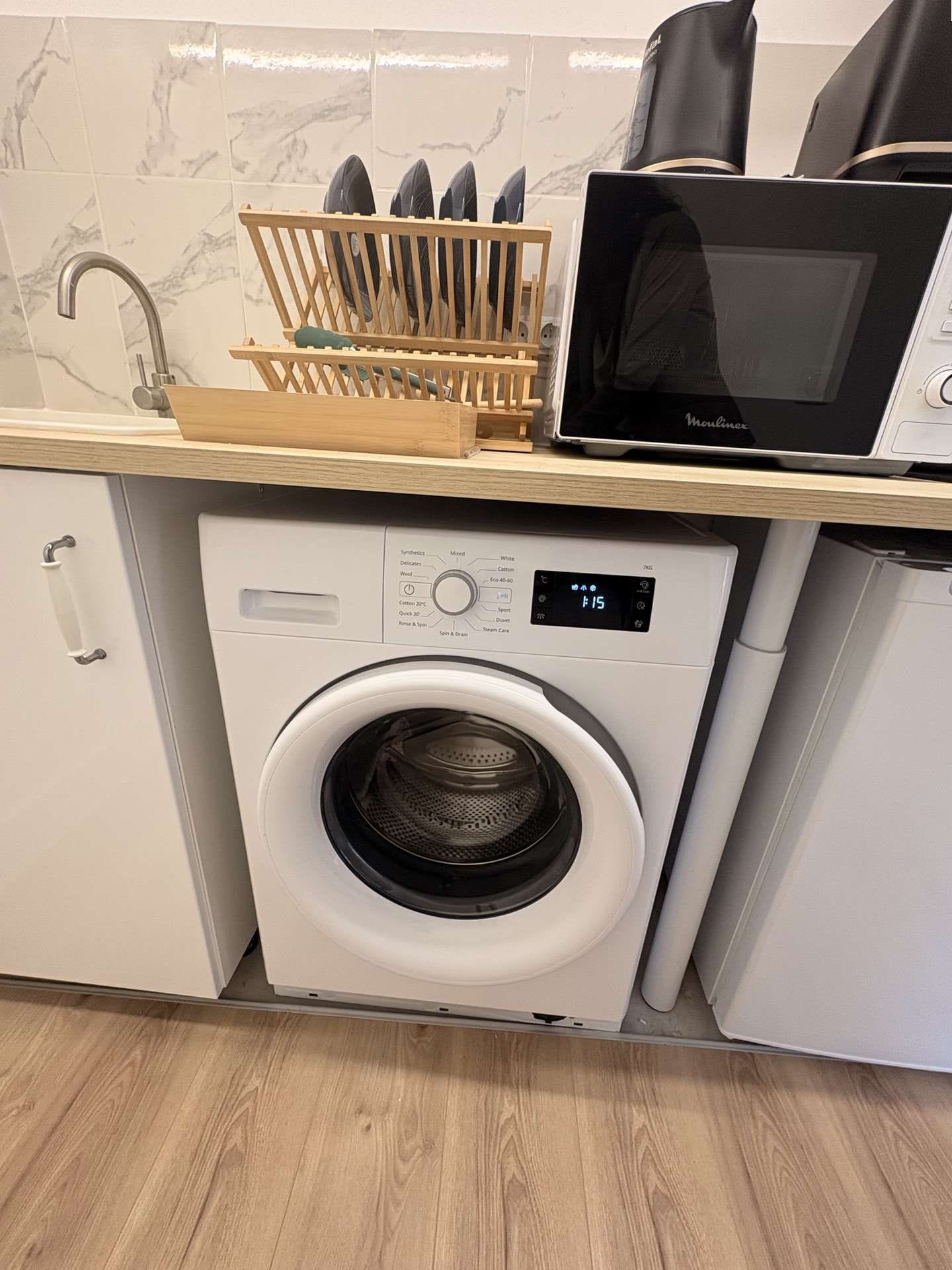 A compact kitchen with a built-in washer and dryer, a microwave, and a utensil holder on the countertop.