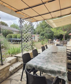 An outdoor patio with a long table, chairs, and a pergola providing shade. - Gîtes de France® - Le Gascou (LALBENQUE)