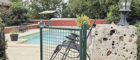 A gated outdoor area with a pool, a wheelchair, and a stone wall.