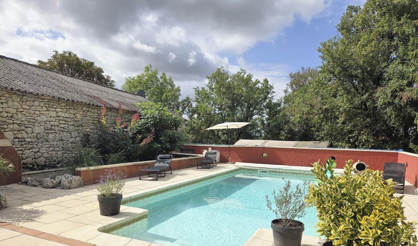 A swimming pool with lounge chairs, a stone wall, and potted plants.