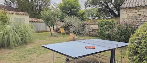 A ping pong table in a backyard with a stone wall, a wooden bench, and a tree.
