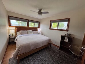 Une chambre à coucher comprenant un lit, une table de chevet, une chaise, une bibliothèque et un ventilateur de plafond.
