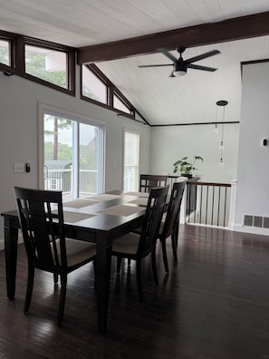 A dining area with a table and chairs, large windows, a ceiling fan, and a staircase leading to an upper level.