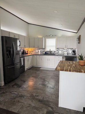 A modern kitchen with white cabinetry, a black refrigerator, and a wooden countertop.