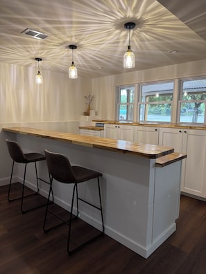 A kitchen with a central island, bar stools, and a view of the outdoors through windows.