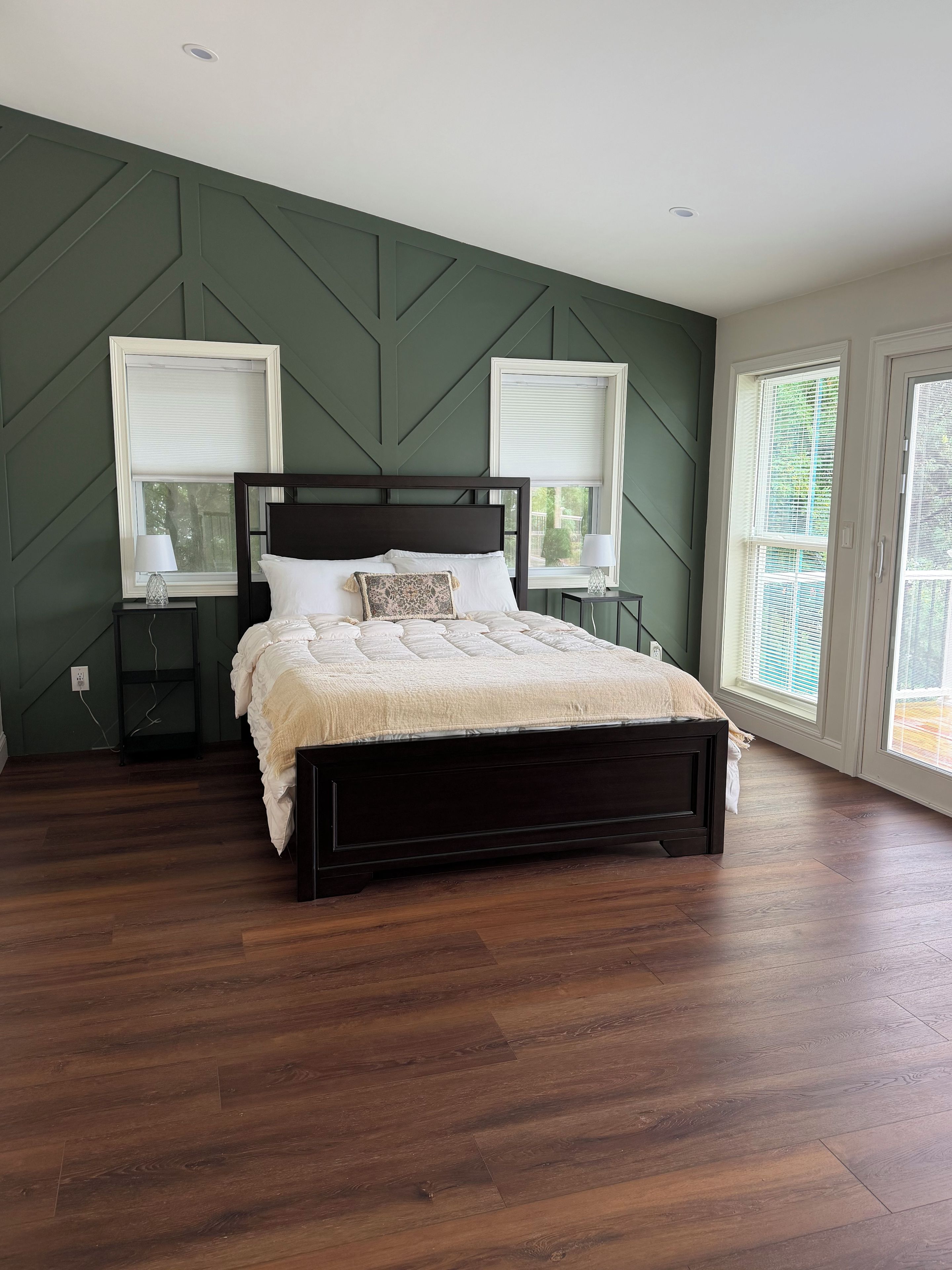 Une chambre avec un grand lit, deux tables de chevet et une fenêtre avec des stores.