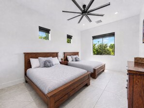 Une chambre avec deux lits, un ventilateur de plafond et des fenêtres donnant sur un paysage verdoyant.