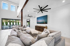 A spacious living area with a modern design, featuring a large sectional sofa, a ceiling fan, and a large painting of a landscape. - Valencia - 35' Ceilings - Private Pool - Biltmore (Phoenix)