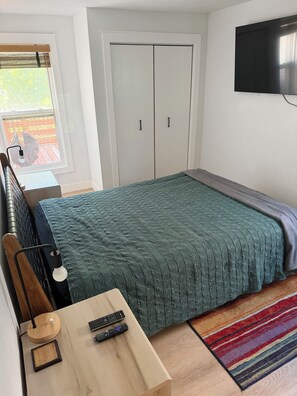 A bedroom with a bed, a desk with a lamp, a TV, and a wardrobe.