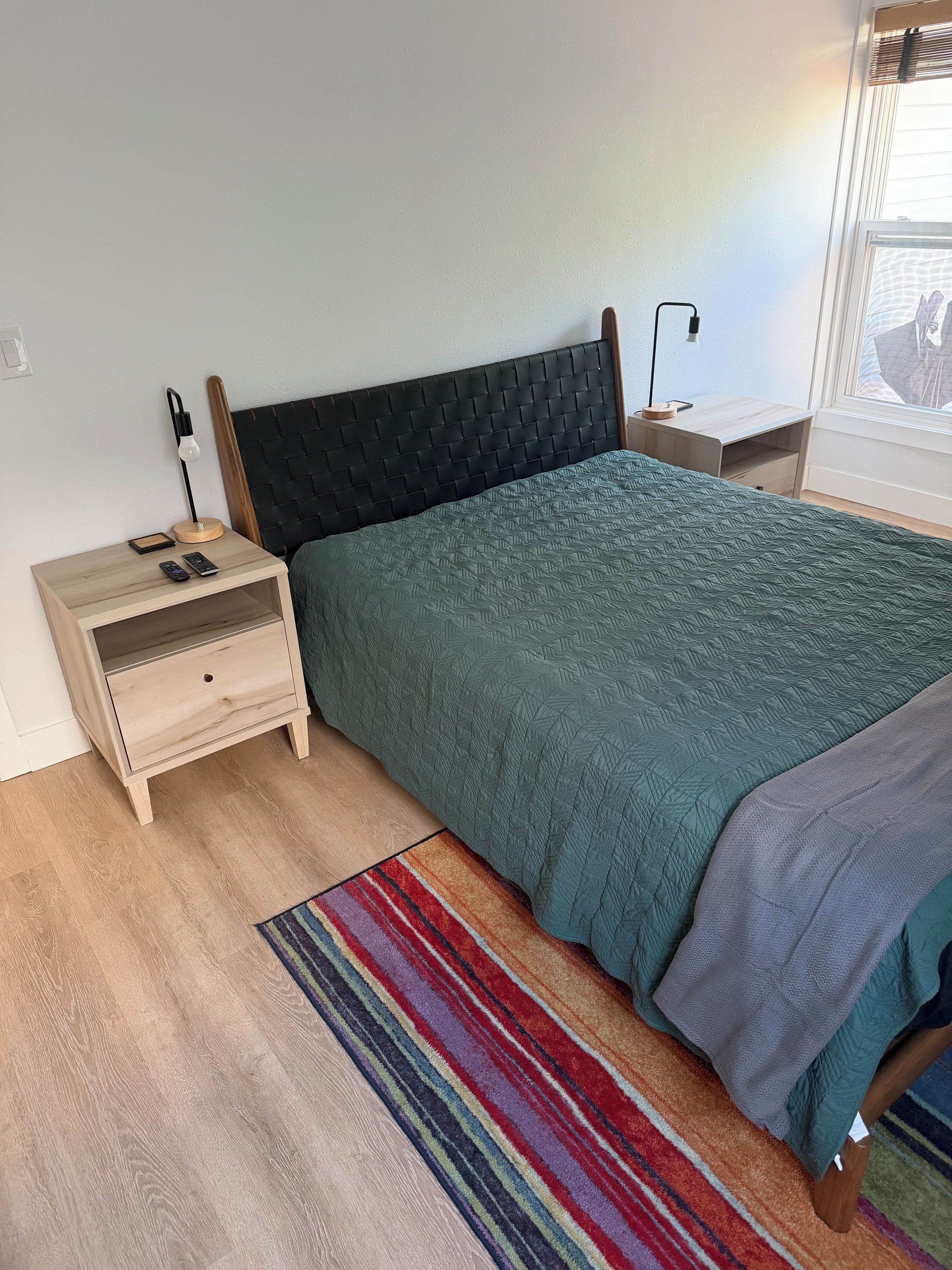 Une chambre à coucher avec un lit, une table de chevet, une lampe et une fenêtre.
