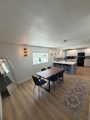 Een moderne keuken met een centraal eiland, een eettafel met stoelen en uitzicht op het landschap door een raam.