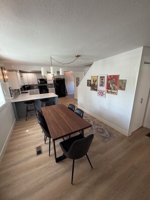 A modern kitchen with white cabinets, a black refrigerator, and a dining area with a wooden table and black chairs. - 5 Minute Walk to Kendrick Park and Main Street - Peace in the Middle of Town! (Sheridan)