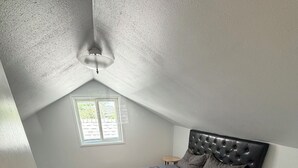 Una camera da letto con un letto, una finestra, un ventilatore a soffitto e un tavolino rotondo.