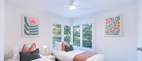 Camera da letto con due letti, una ventola a soffitto e opere d'arte alle pareti.