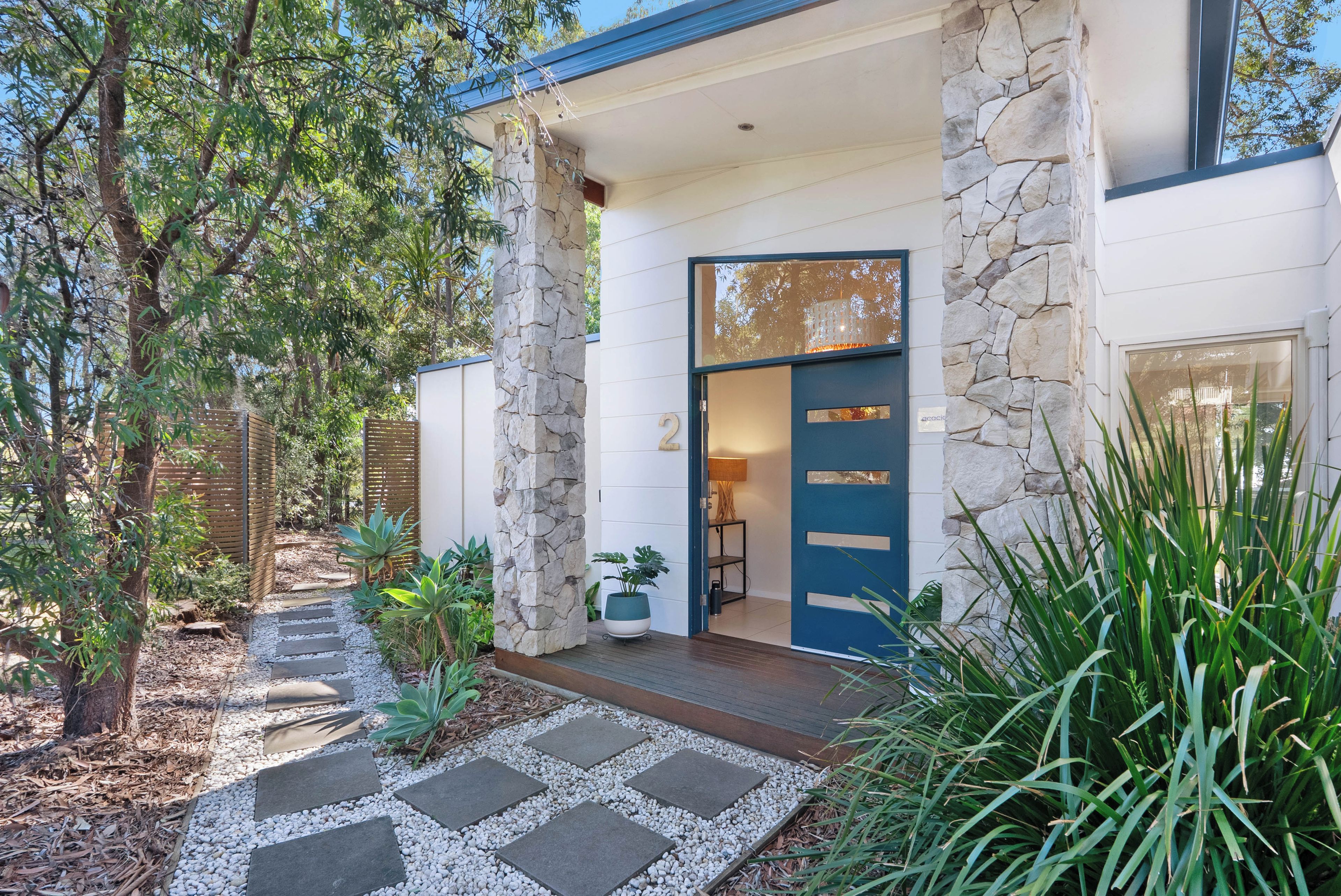 A modern house with a stone facade, a blue door, and a garden with a stone pathway.