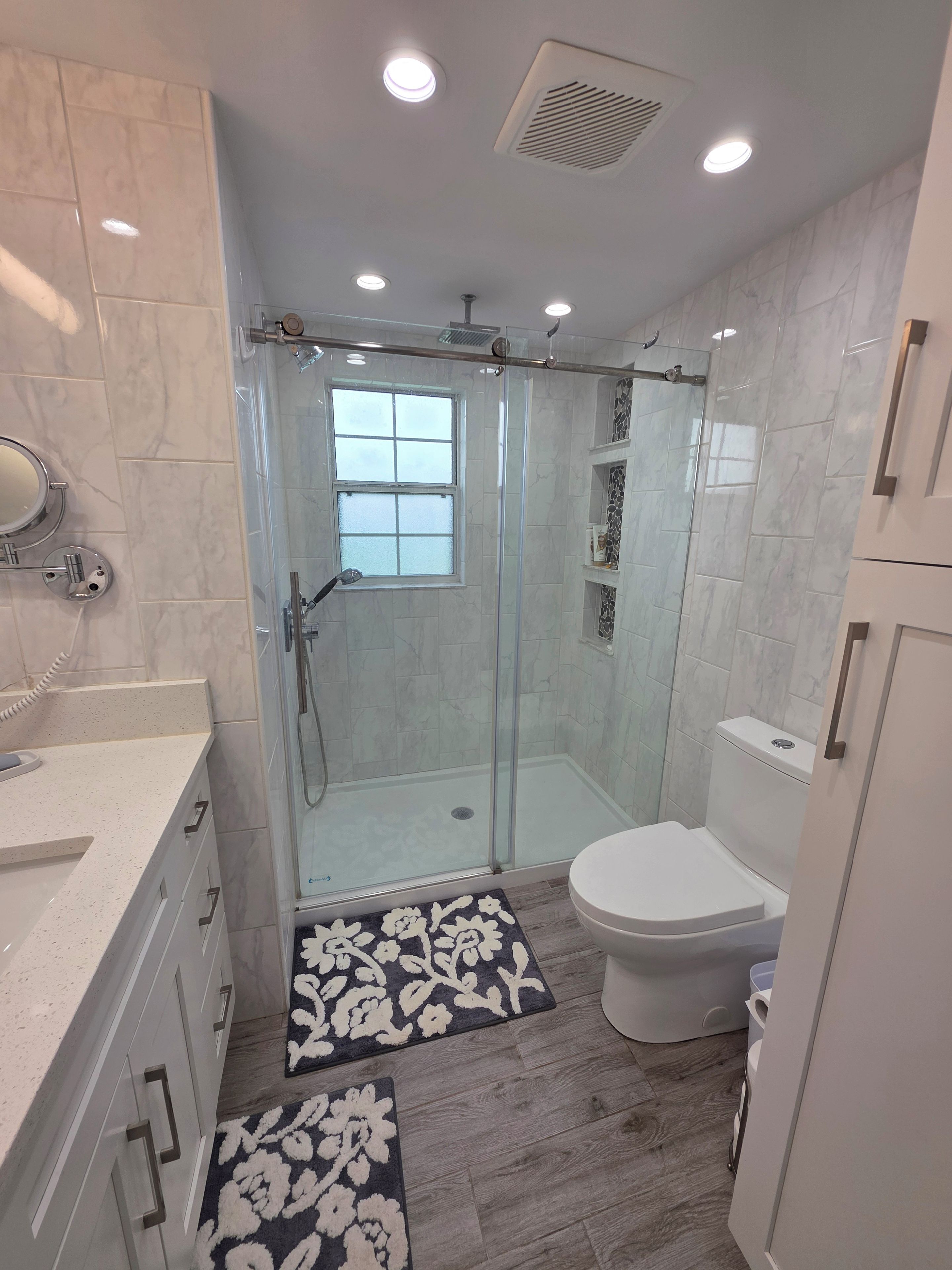 A modern bathroom with a glass-enclosed shower, a toilet, and a sink with a mirror.
