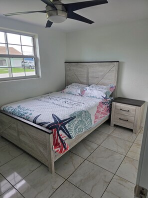 Ein Schlafzimmer mit einem Bett, einem Nachttisch, einem Deckenventilator und einem Fenster mit Blick nach draußen.