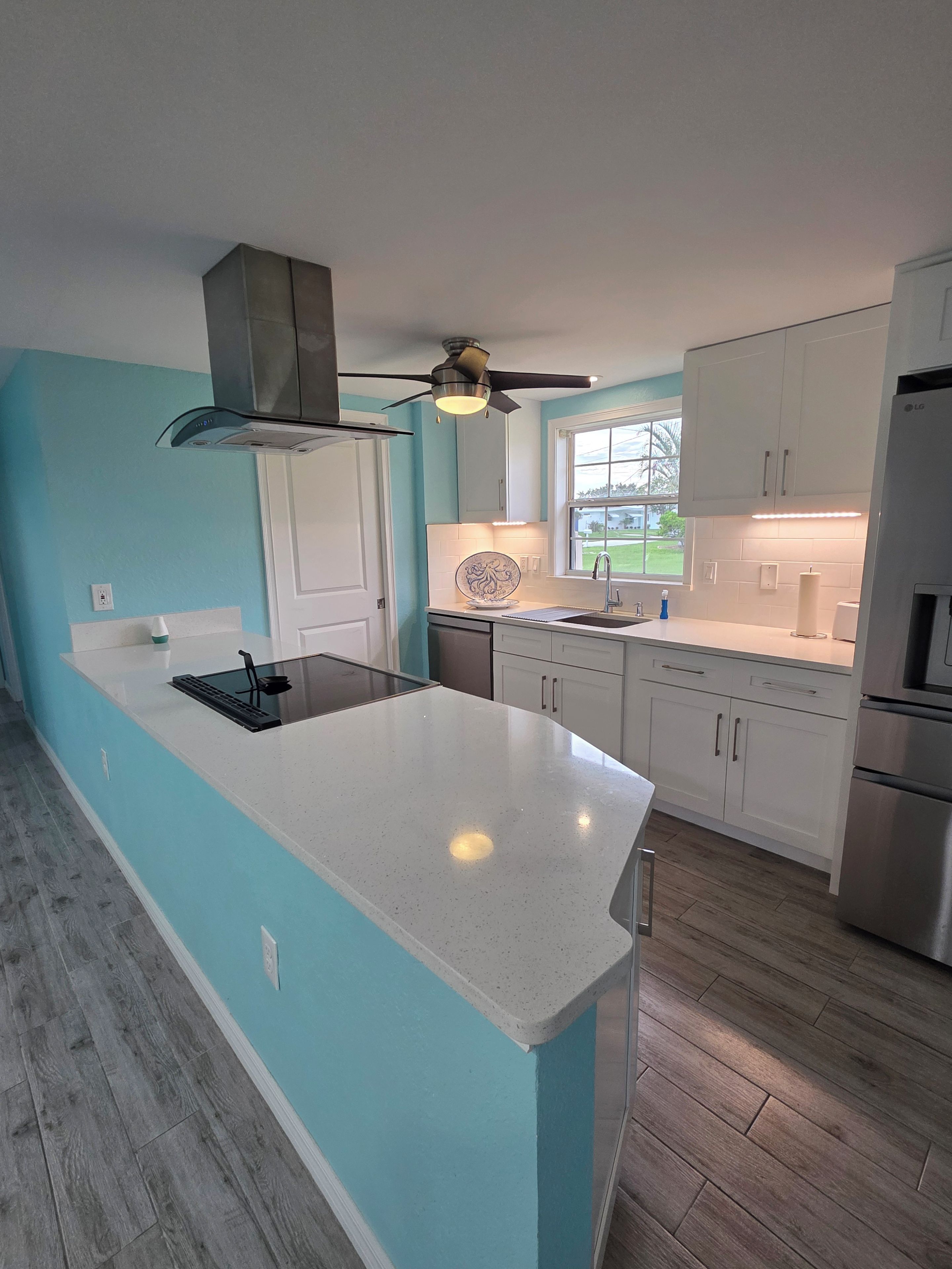 A modern kitchen with a central island, white cabinetry, and a ceiling fan.