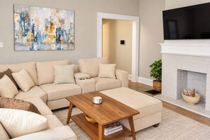 A living room with a beige sectional sofa, a wooden coffee table, a fireplace, and a television. - Cincy 5BR Retreat | Xavier + Zoo | Sleeps 7 (Cincinnati)