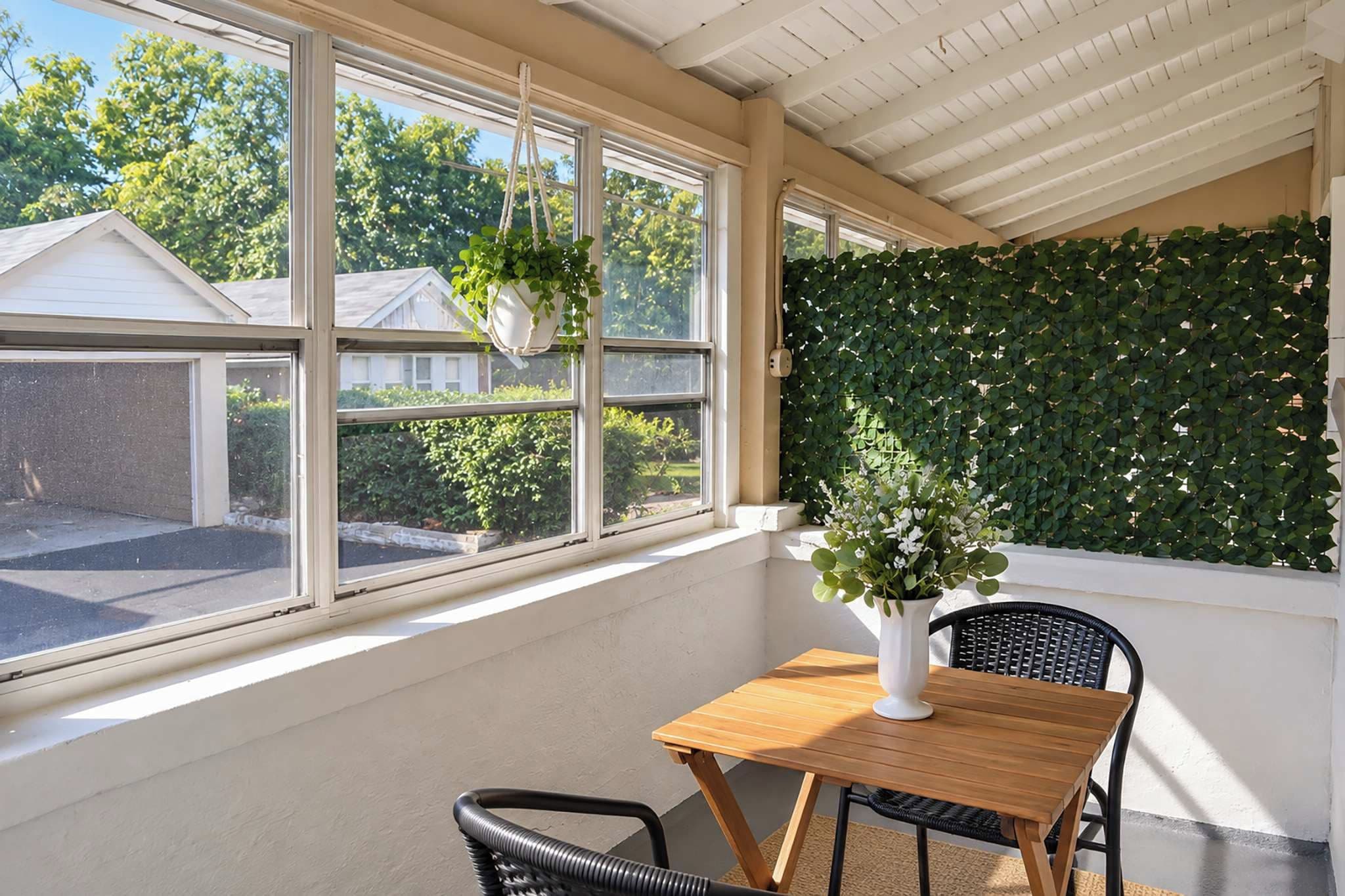 A sunlit room with a table and chairs, a hanging plant, and a wall covered in foliage.