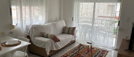 Una habitación con un sofá blanco, una mesita, un tapete estampado y un ventilador de techo.