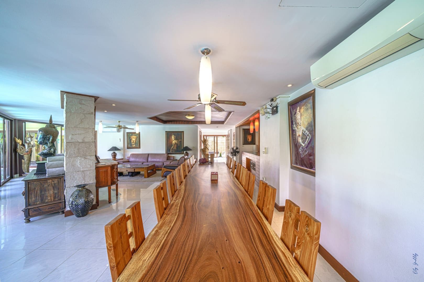 A spacious dining area with a long wooden table and chairs, a ceiling fan, and artwork on the walls.