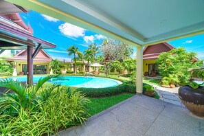 Área de piscina com piscina circular, rodeada por plantas tropicais e palmeiras.