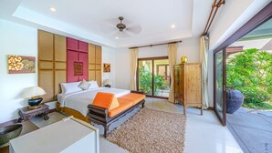Ein geräumiges Schlafzimmer mit einem großen Bett, einem Deckenventilator und Blick auf einen üppigen Garten durch eine Glastür.