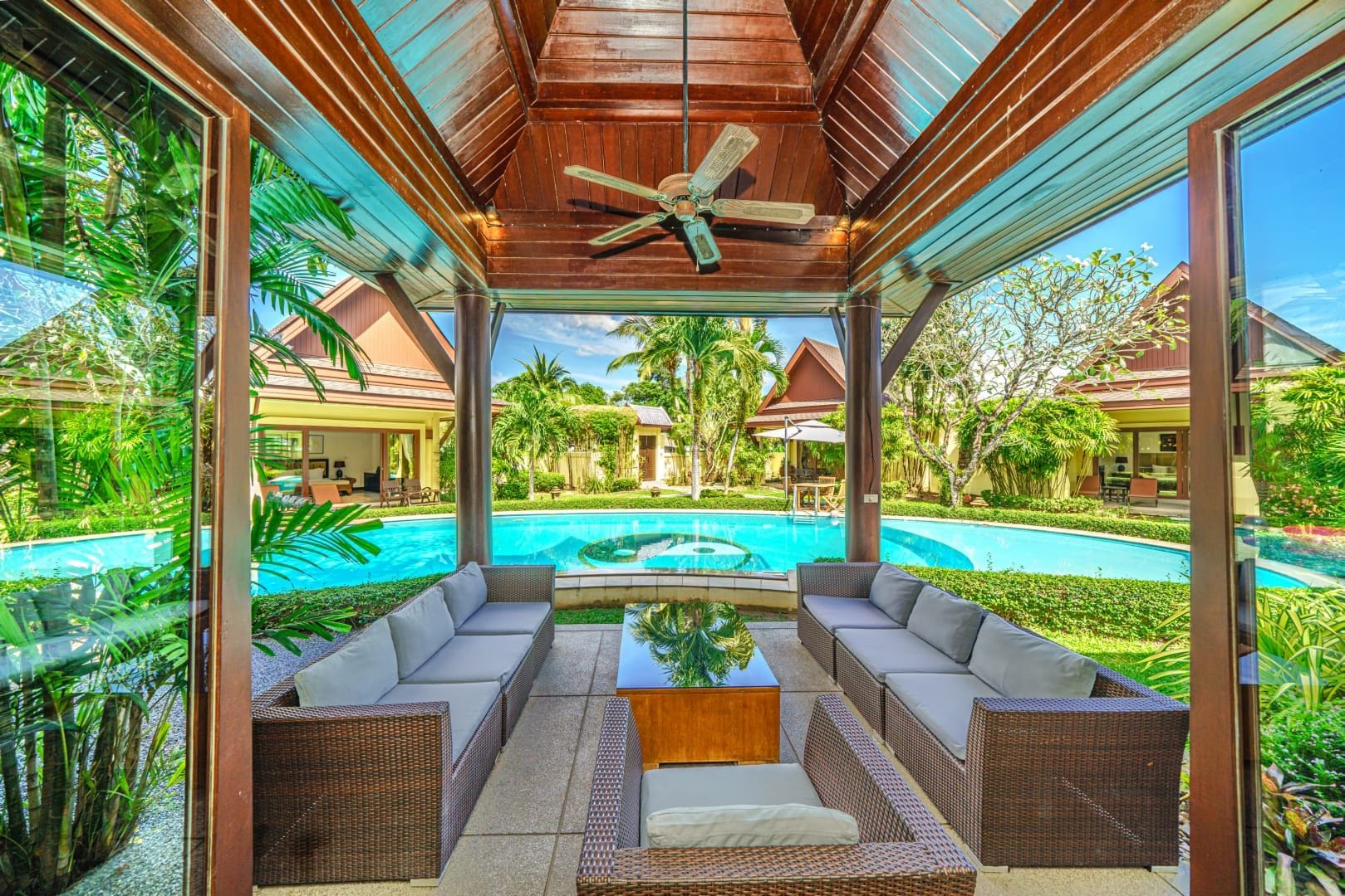A covered outdoor seating area with a pool in the background.