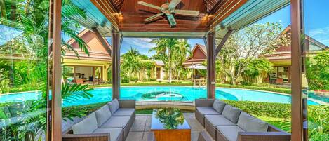A covered outdoor seating area with a pool in the background.