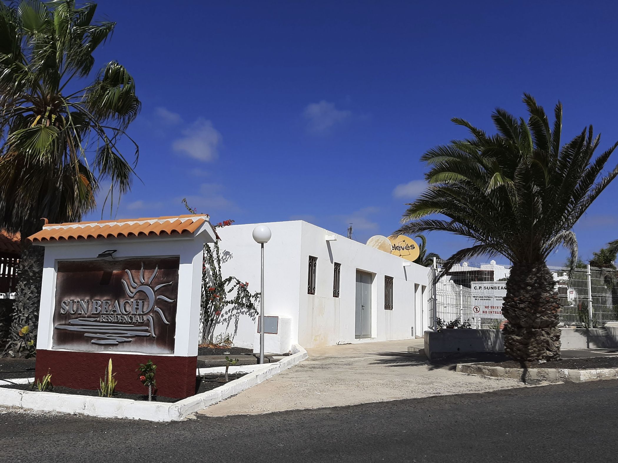 Zona residencial con un edificio blanco, un letrero de Sunbeam Residential y una palmera.