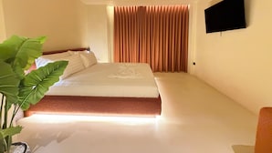 Ett hotellrum med en säng, en platt-TV som är monterad på väggen och en stor krukväxt.