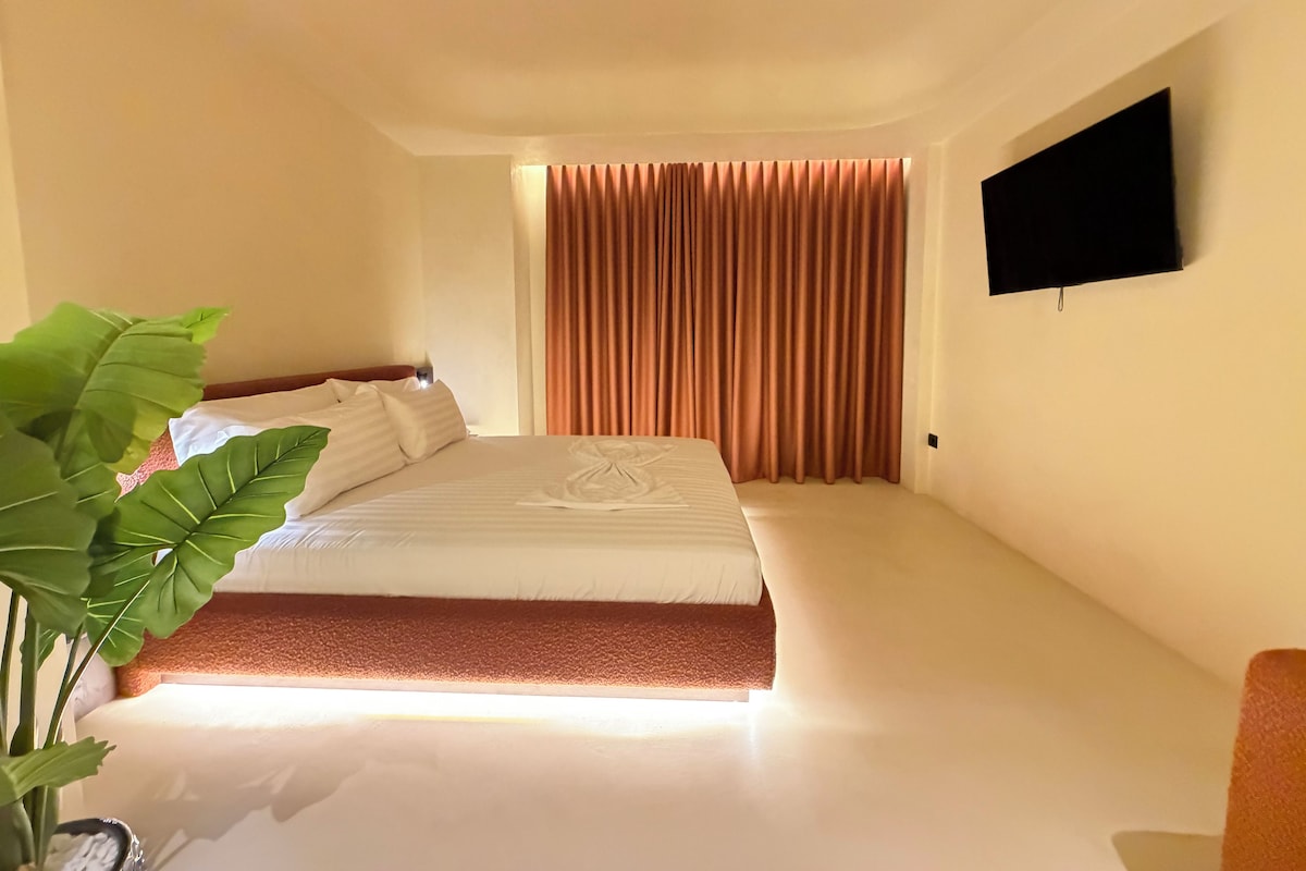 A hotel room with a bed, a flat-screen TV mounted on the wall, and a large potted plant.