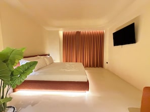 A hotel room with a bed, a flat-screen TV mounted on the wall, and a large potted plant. - Luxuria Suites (Tiranë)
