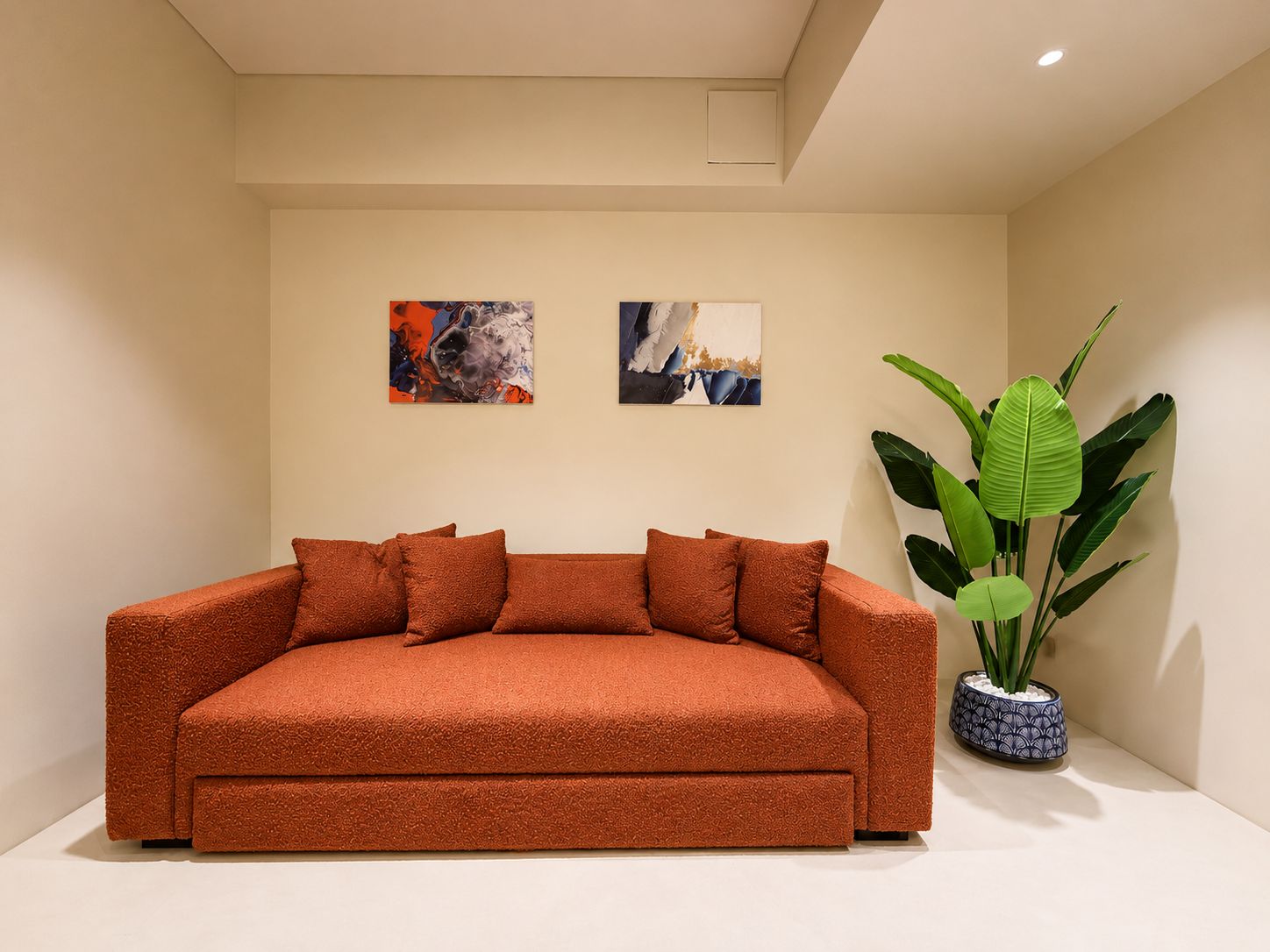 Una sala moderna con sofá, dos cuadros abstractos y una planta verde grande.