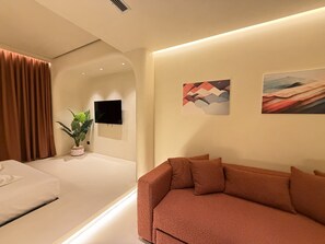 A modern living room with a sofa, a flat-screen TV mounted on the wall, and a potted plant. - Luxuria Suites (Tiranë)