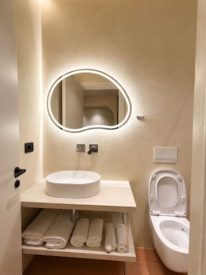 A bathroom with a round mirror, a sink, and a toilet. - Luxuria Suites (Tiranë)