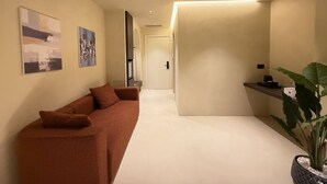 En hall med en soffa, konstverk, en växt och en kaffemaskin.