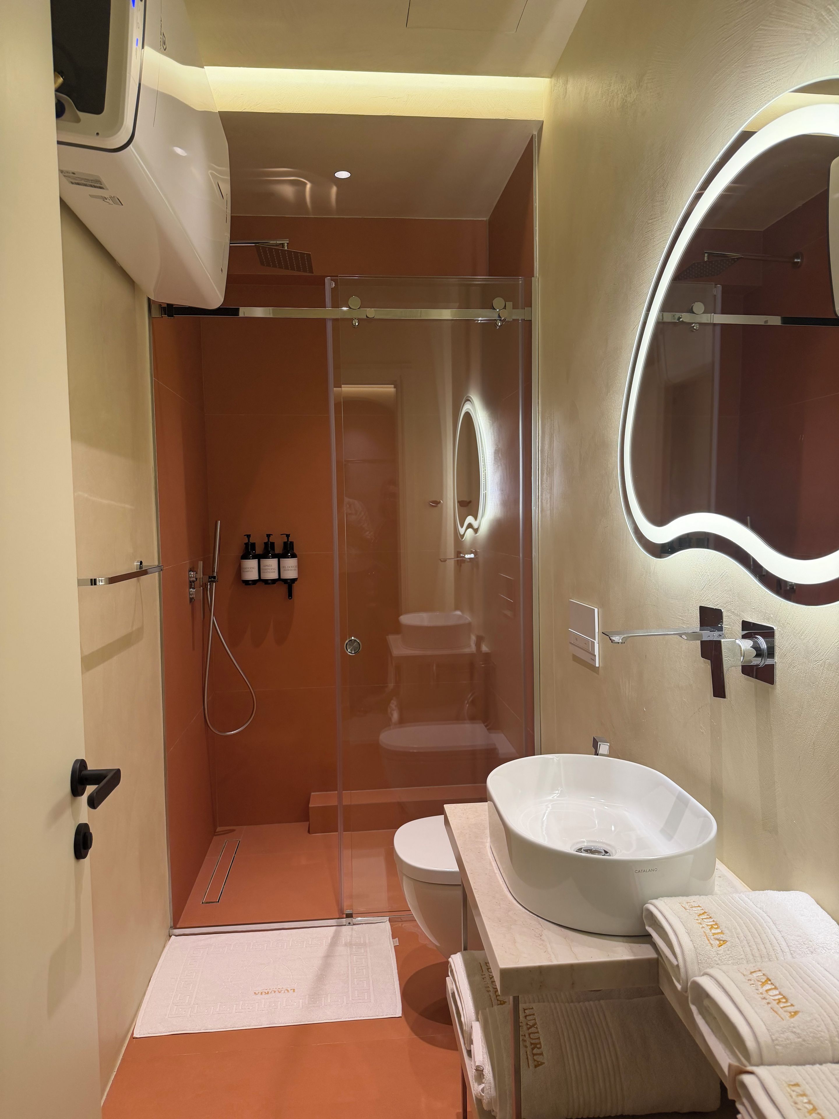 A modern bathroom with a glass-enclosed shower, a white sink, and a large mirror with built-in lighting.
