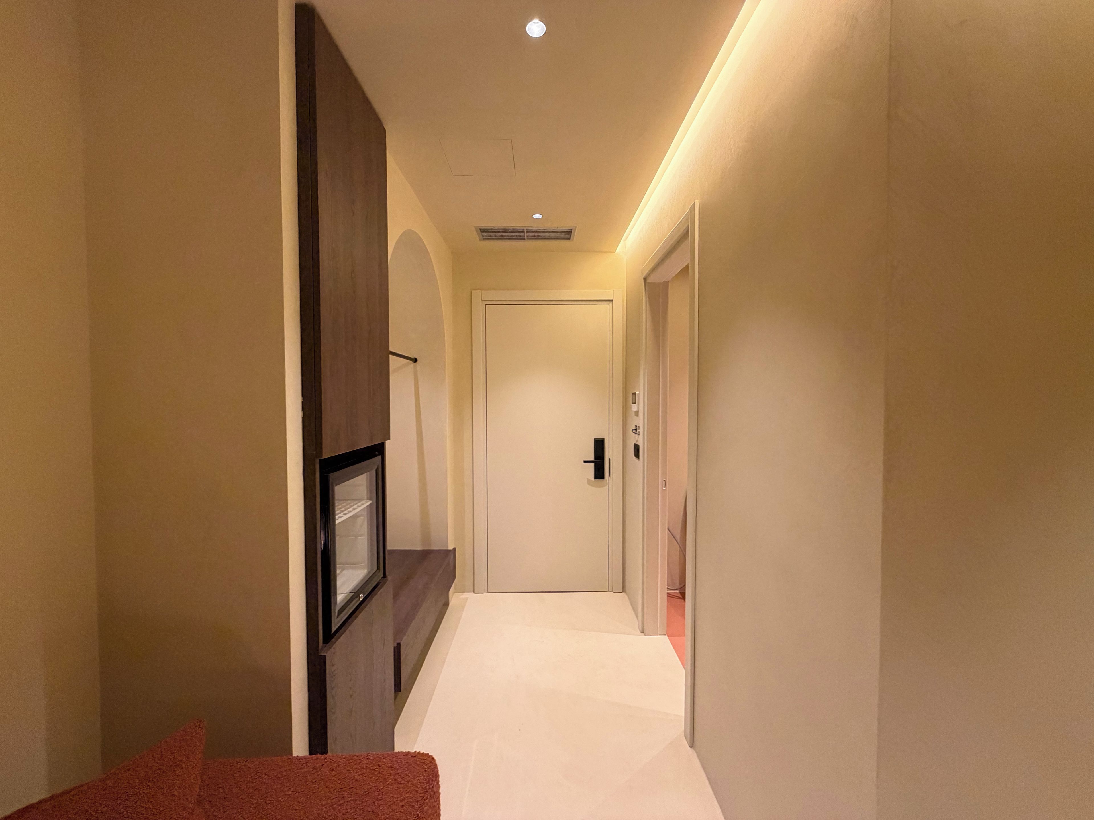 A narrow hallway with a door at the end, a framed picture on the left, and a light strip along the ceiling.