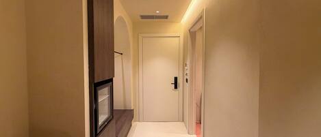A narrow hallway with a door at the end, a framed picture on the left, and a light strip along the ceiling.