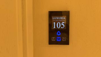 Pantalla digital para 'LUXURIA SUITES 105' con iconos que indican 'No molestar', 'Ocupado' y 'Limpiar habitación'.