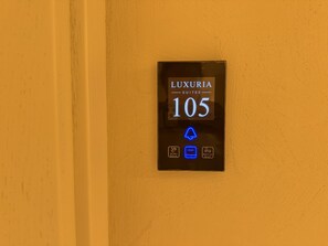 A digital display for 'LUXURIA SUITES 105' with icons indicating 'Do Not Disturb,' 'Occupied,' and 'Make Up Room.' - Luxuria Suites (Tiranë)