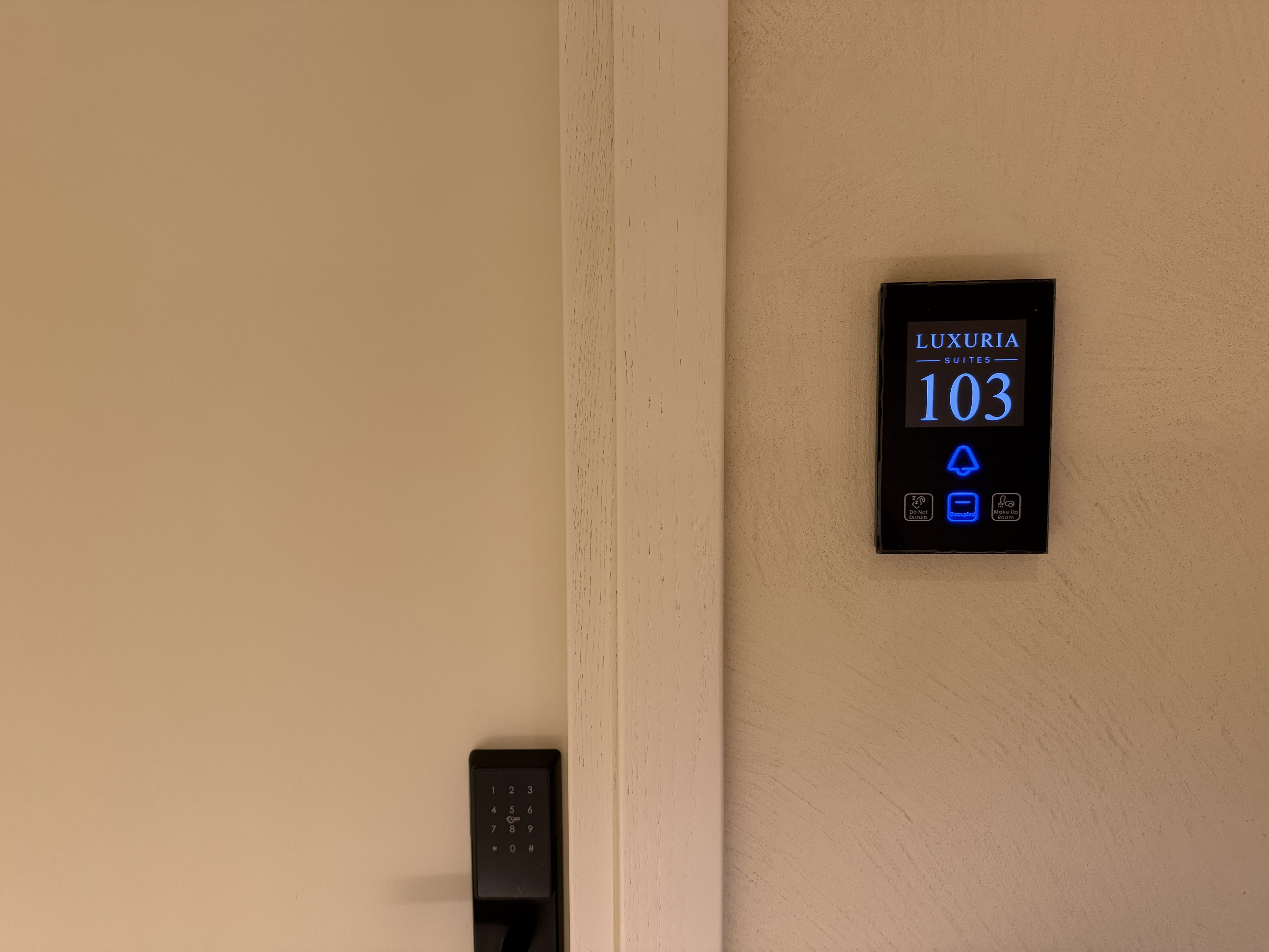 Pantalla digital en una pared que indica el número de habitación 103 en un hotel llamado LUXURIA.