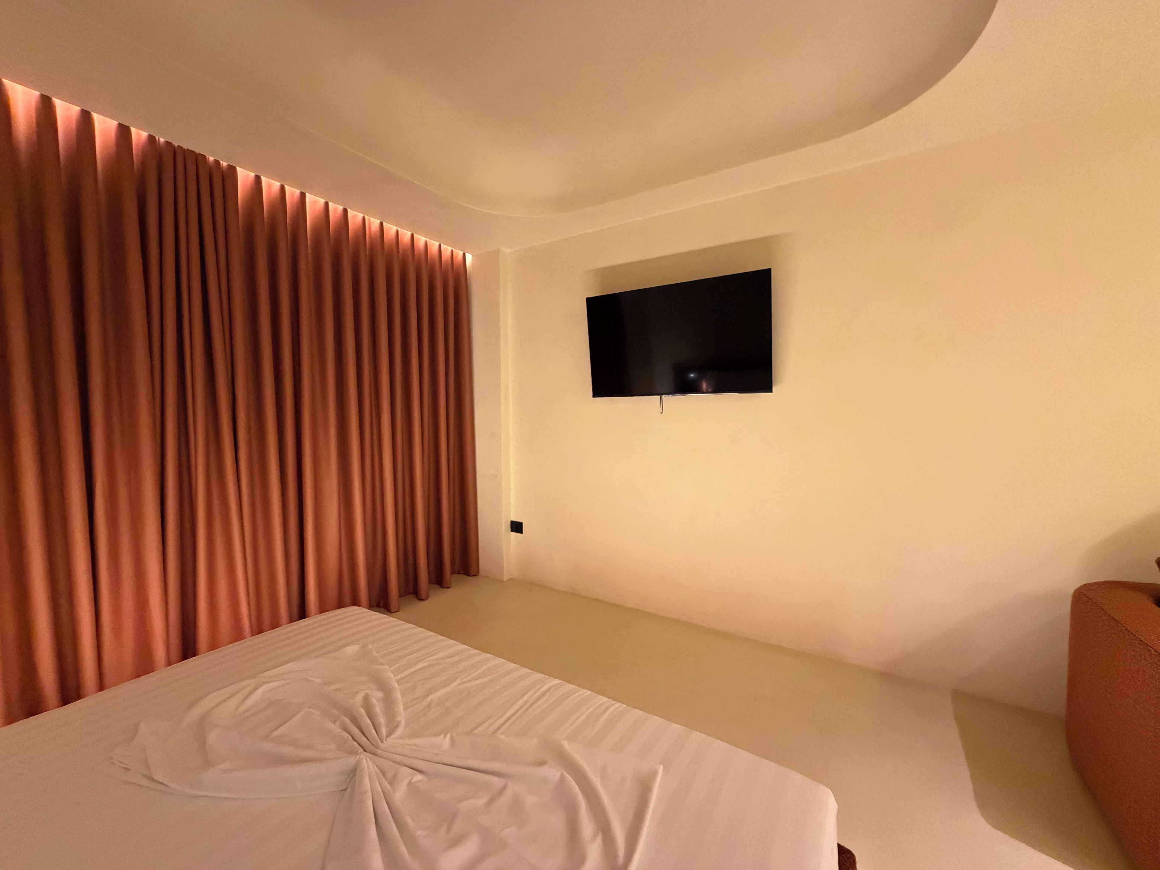 A hotel room with a bed, a television mounted on the wall, and a curtain.