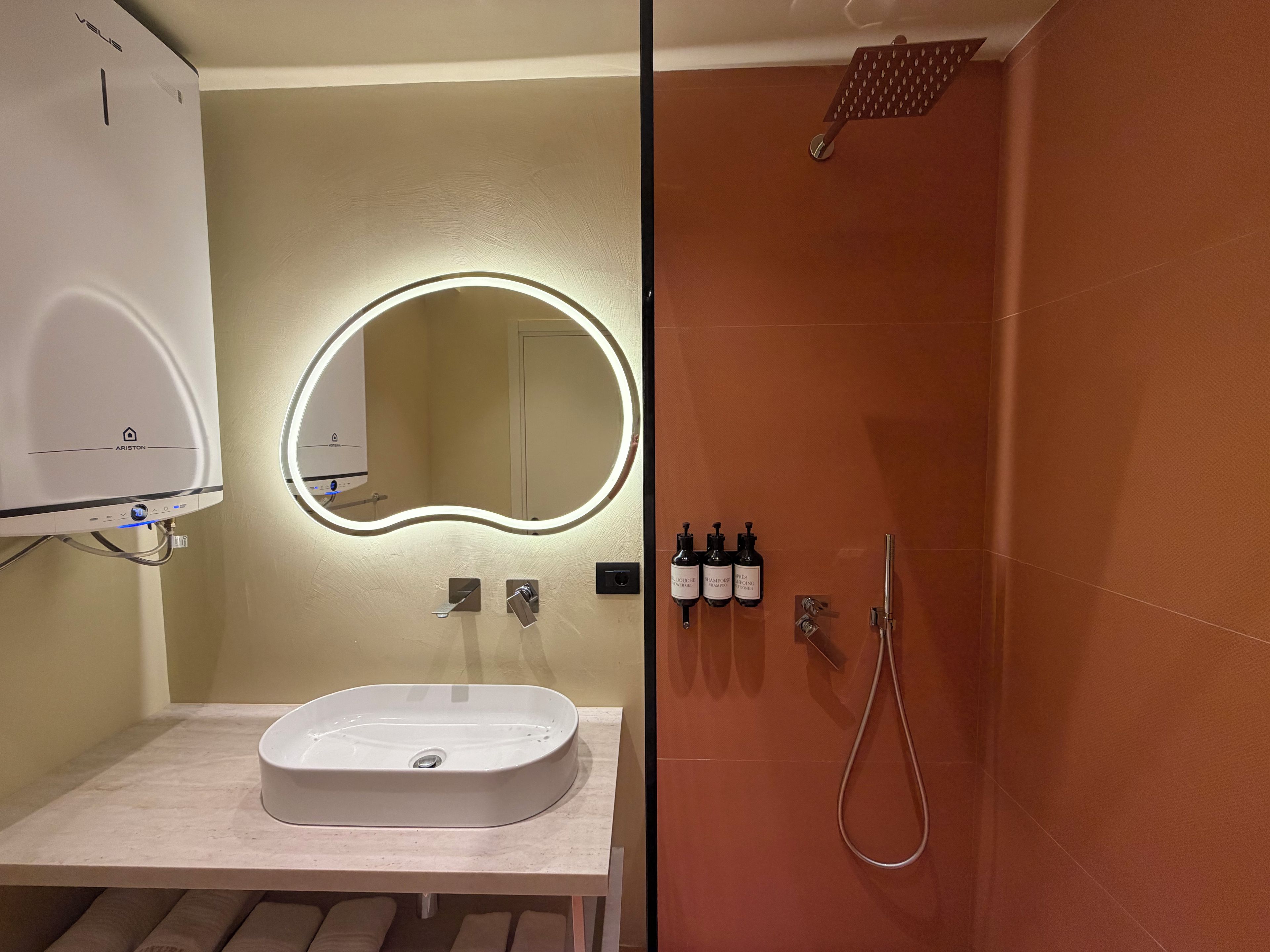 Un baño con lavamanos blanco, un espejo con luz y una ducha, además de artículos de aseo en la pared.