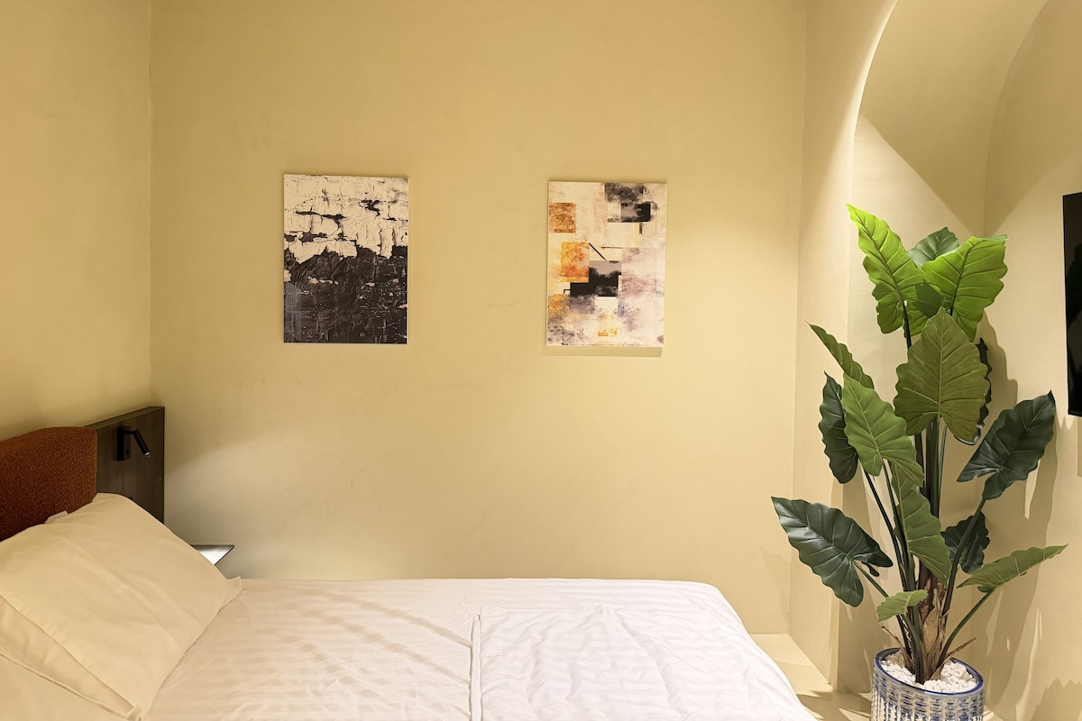 A bedroom with a bed, two wall art pieces, and a potted plant.